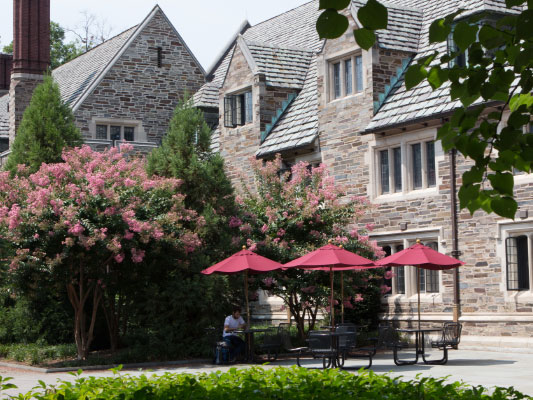 Three outdoor tables with red umbrellas set up alongside Princeton University campus